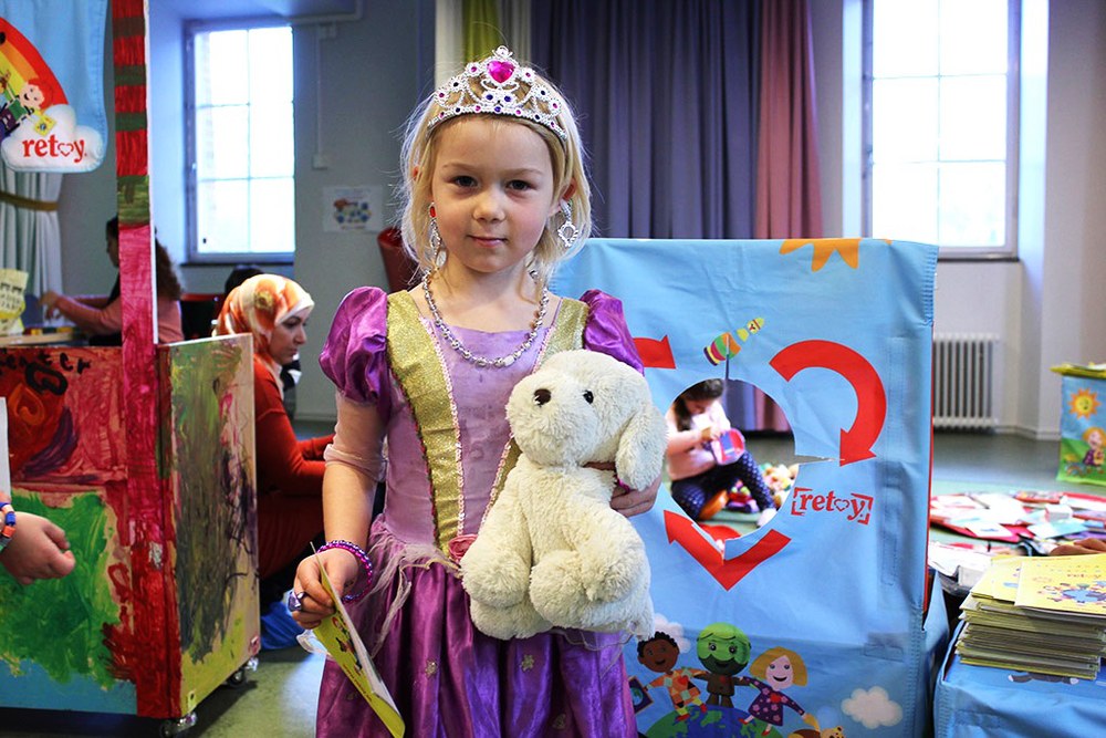 A child in a princess dress holding a soft toy at a toy swap