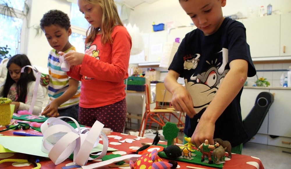 Children crafting with paper and reused toys at a table